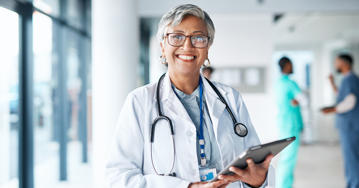 a female doctor smiling short gray hair and glasses holding a tablet in the hospital