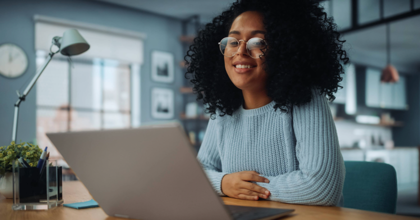 african-american woman smiling sitting at her desk looking at her laptop