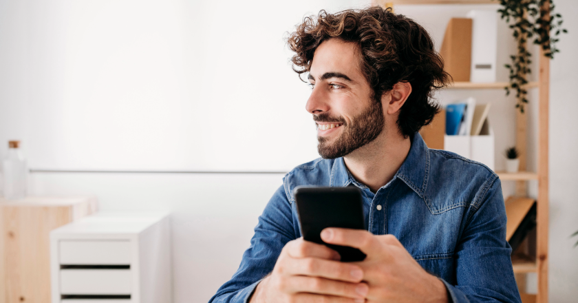 man smiling in his 30s holding his phone and looking somewhere else
