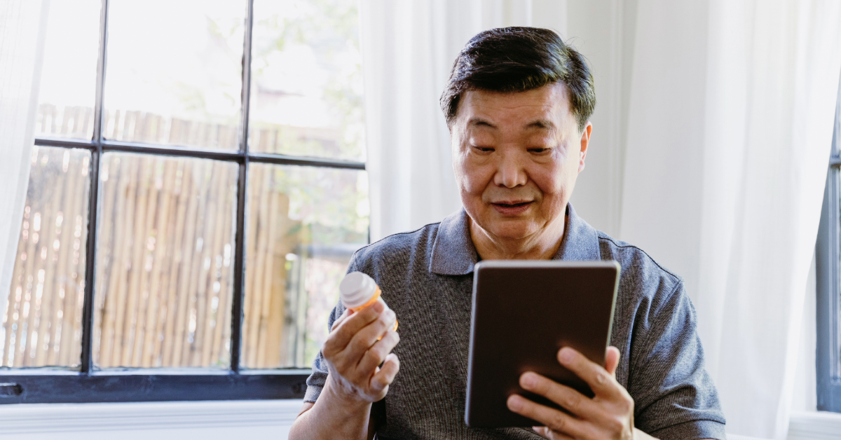 older asian male looking at his tablet and holding medication