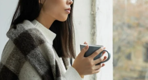young asian woman looking through the window and holding a mug