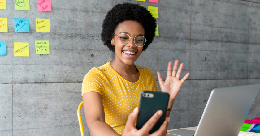 young woman on her laptop holding her phone on a video call